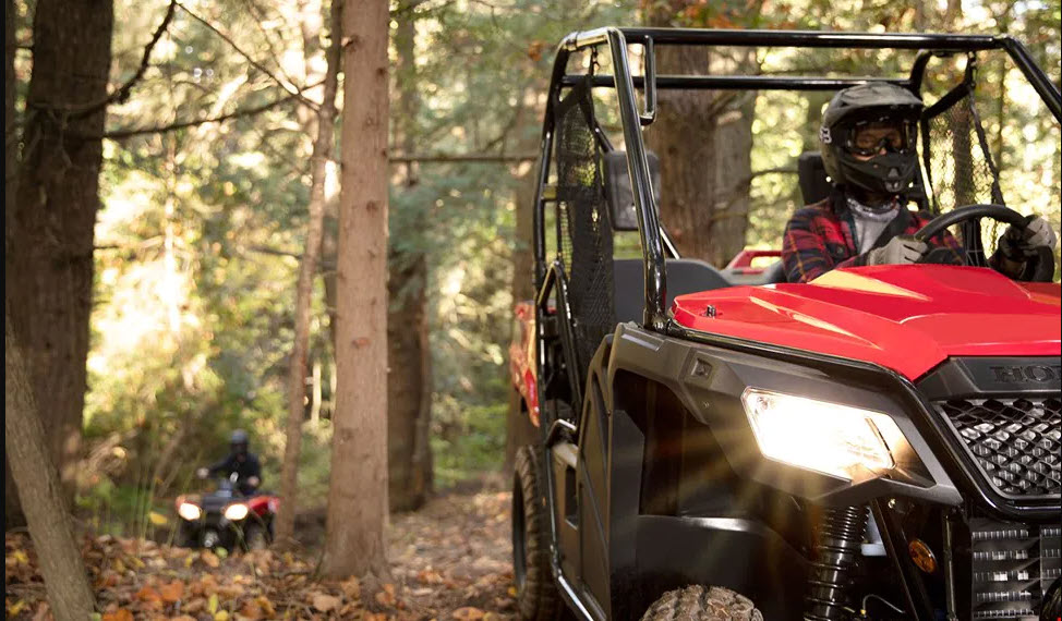 Véhicule côte-à-côte Honda rouge conduisant sur un chemin en forêt avec un VTT Honda rouge en arrière-plan / Red Honda SxS driving on a forest path with a Red Honda ATV in the background