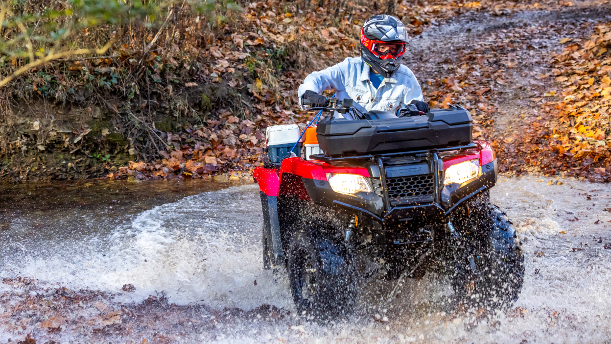 Front facing image of driver on rancher coming out of puddle. Dirt road in background.