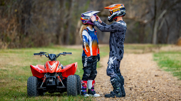 Young rider with Adult rider holding their helmet. Beside ATV.