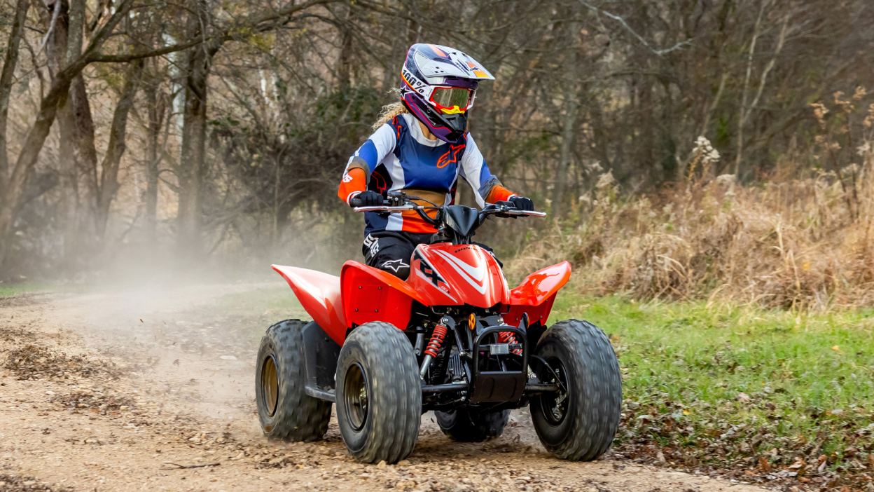 Young Rider on ATV in woods. Trees in background.