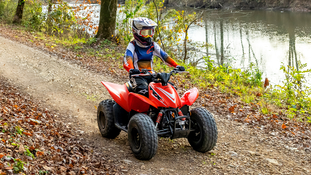 Young Rider on ATV in woods on dirt track. River in background