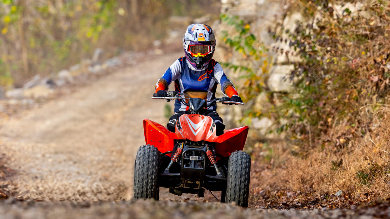 Young rider on ATV on dirt road. Front facing.