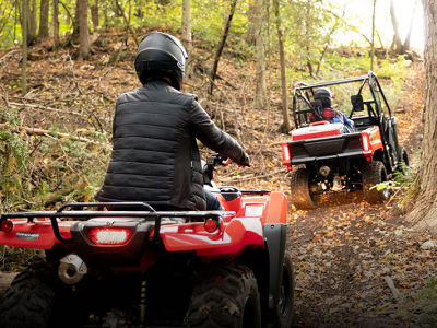 Riders in a Honda SxS and a on a Honda ATV riding on a trail in safety gear 