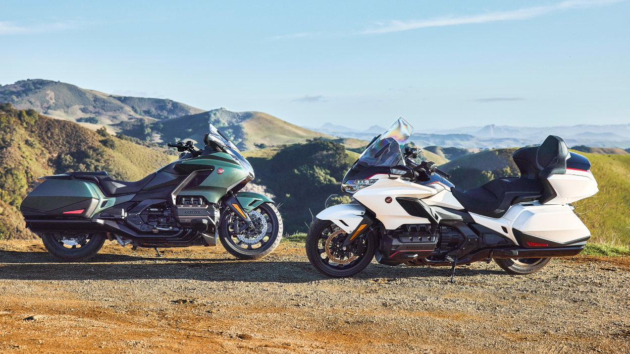 Green bike on the left facing white bike on the right. Green hills in background.