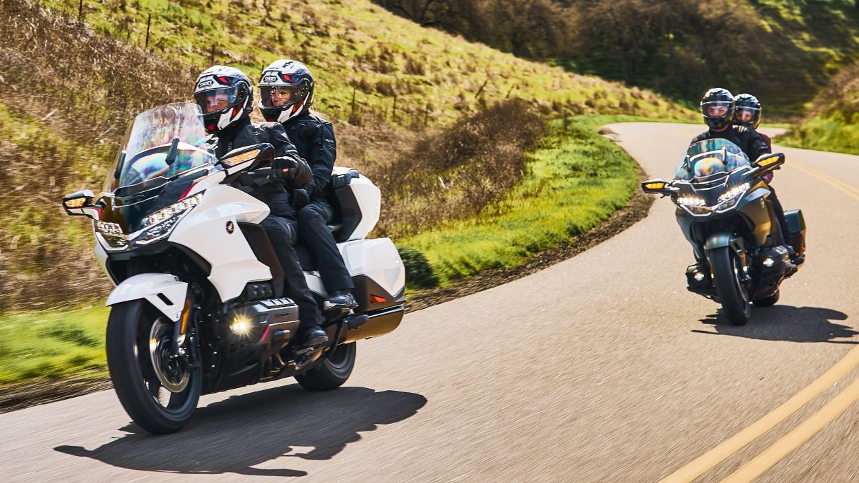 Deux coureurs sur vélo blanc devant deux coureurs sur vélo vert sur route. Collines en arrière-plan.