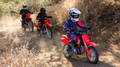 Three young riders on dirt track. Rider in front has a White helmet on.