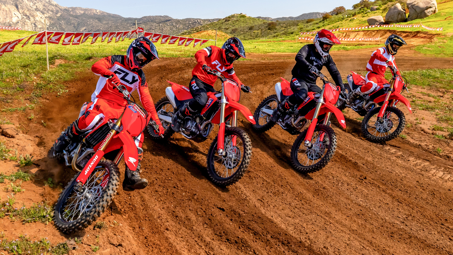 Lineup of four riders making left turn on dirt track.