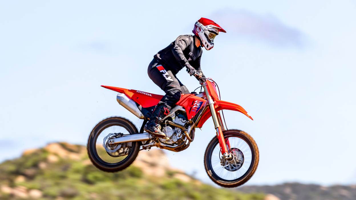 Pilote sur une moto tout-terrain en plein vol, face à droite.