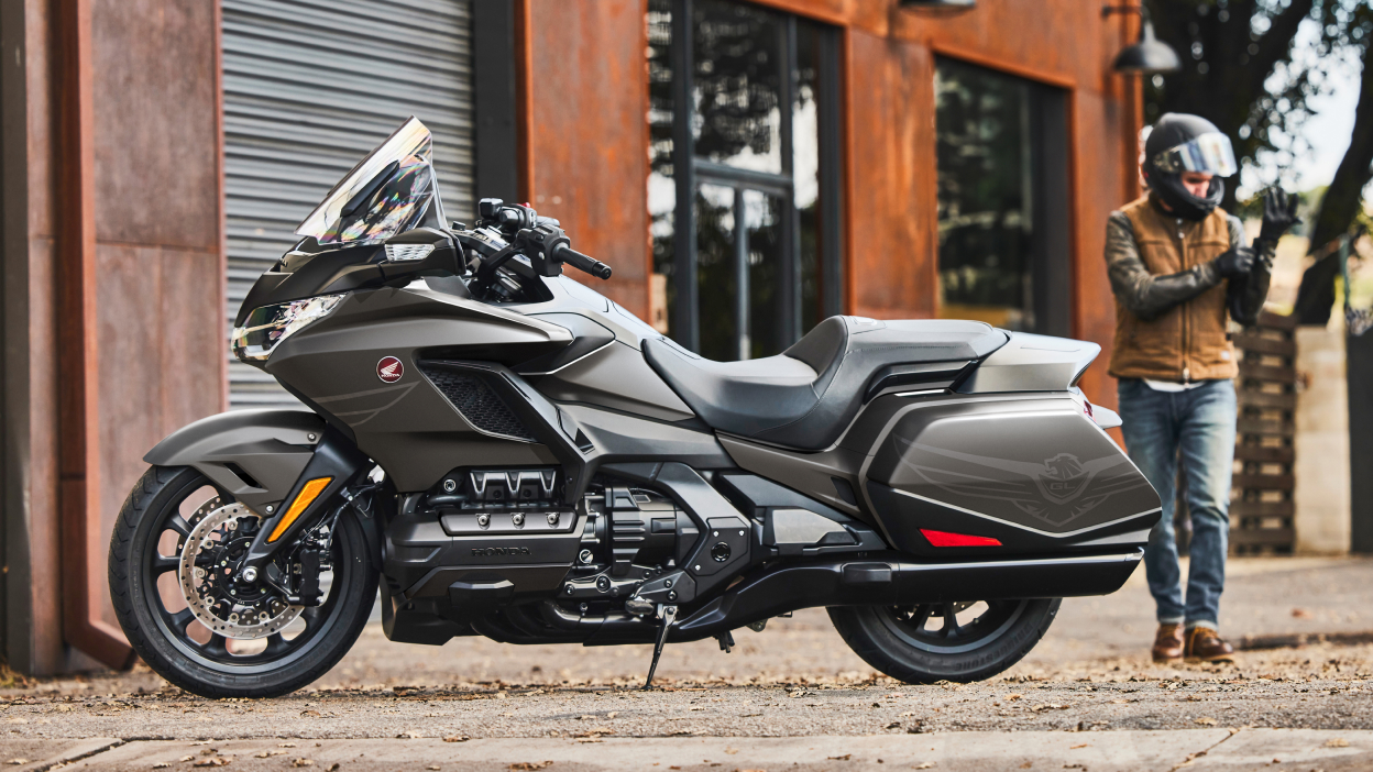 Image fixe de l'aile Gold Wing devant un bâtiment rouge. Une personne casquée se dirige vers l'aile Gold Wing en arrière-plan.