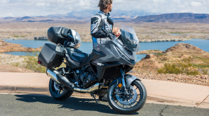 NT1100 stationary, right facing. Rider behind NT1100. Field and lake in background.