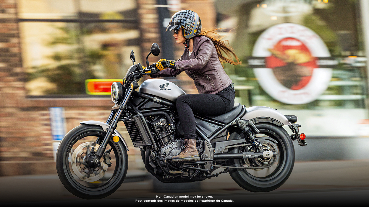 Un motard tourne à droite dans la rue. Bâtiments et voiture garée en arrière-plan. Modèle accessorisé montré.