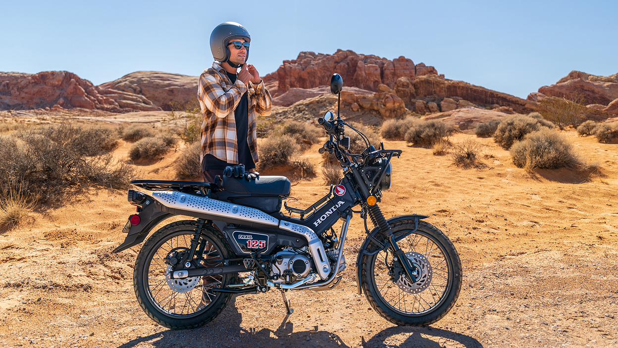 Rider standing behind Trail 125. Trail 125 stationary in desert landscape.