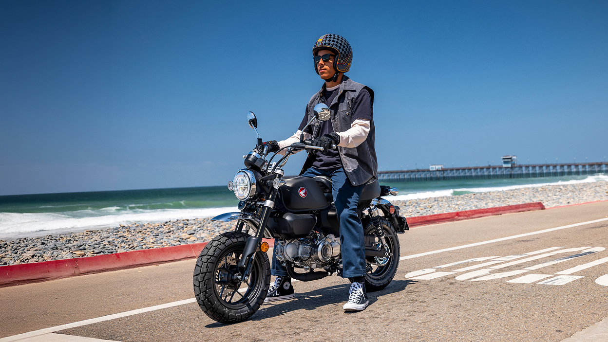 Motard à moto. À l'arrêt sur la route, face à gauche. Plage en arrière-plan.