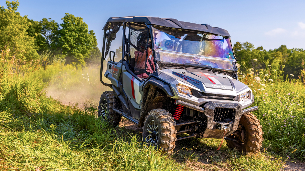 Pioneer right facing on dirt road. Green trees and bushes in background. Dust from back tires.